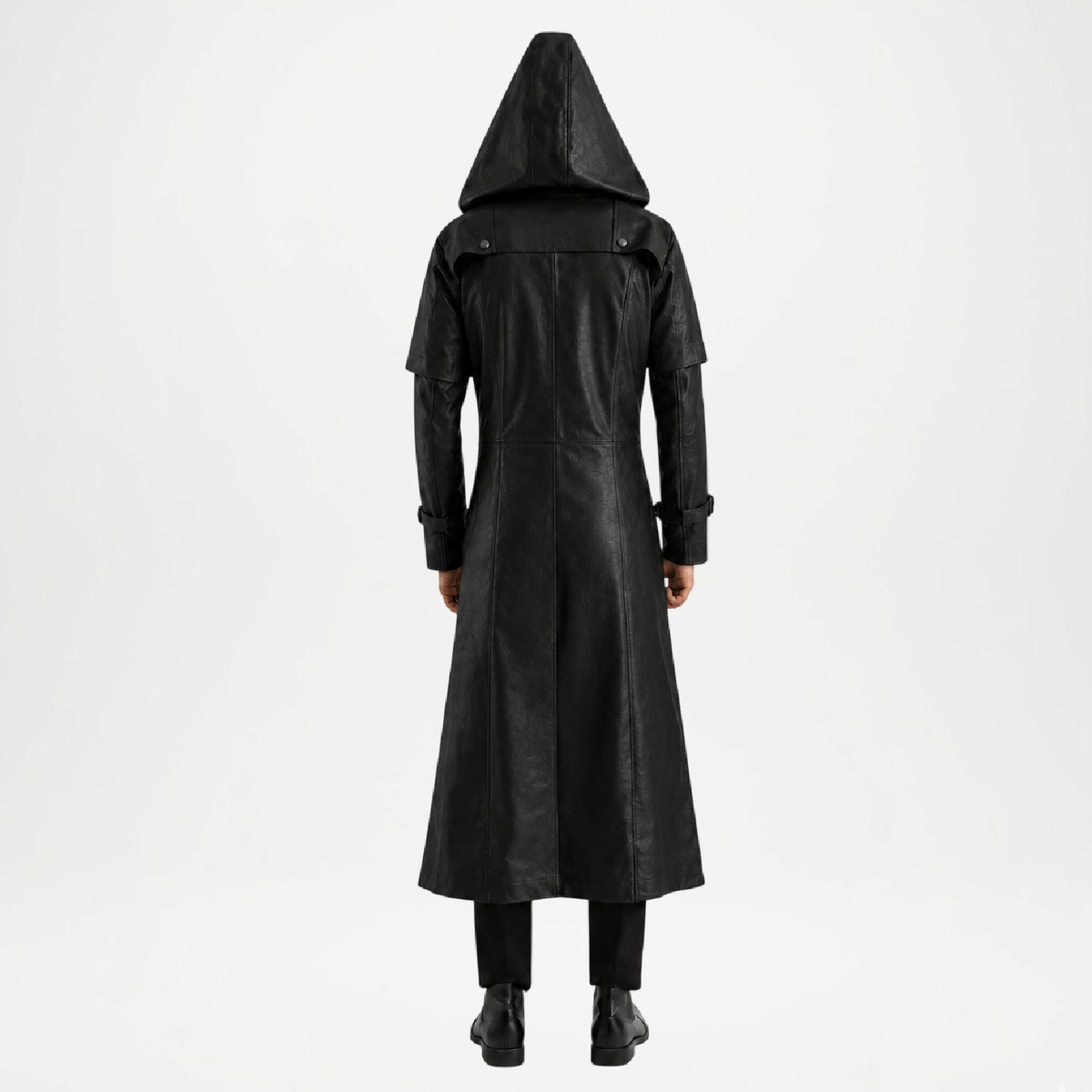 A person viewed from the back wearing a long black hooded coat over black pants and black boots, standing against a plain light gray studio background.