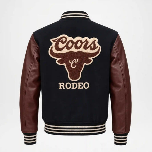 Back view of a varsity-style leather jacket with dark brown leather sleeves and ribbed black, white, and beige striped collar, cuffs, and hem. The back features a large Coors Rodeo embroidered bull head logo in brown and beige.