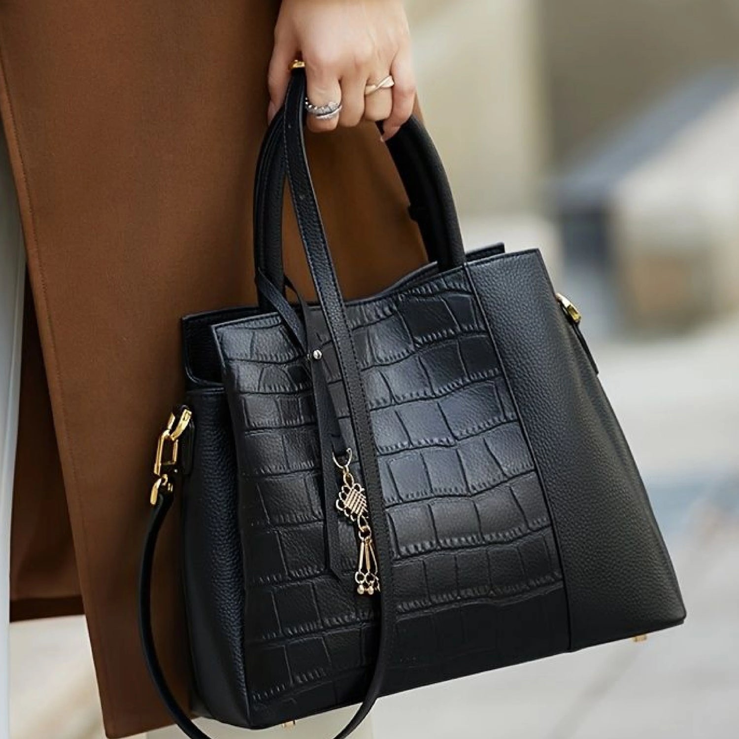 Black croc-embossed leather tote bag with gold hardware, held by hand with rings, stylish women's accessory
