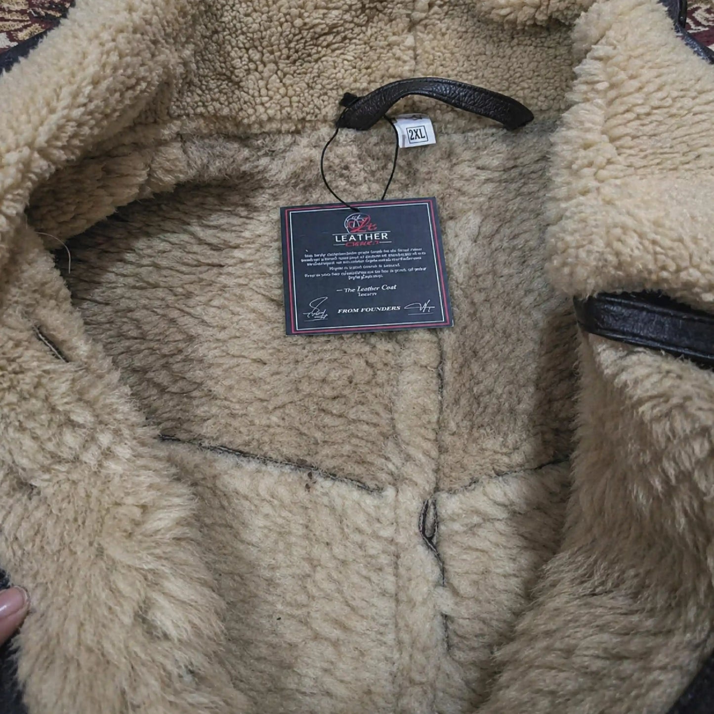 Close-up of a beige sherpa-lined jacket with a brand tag on a textured surface.