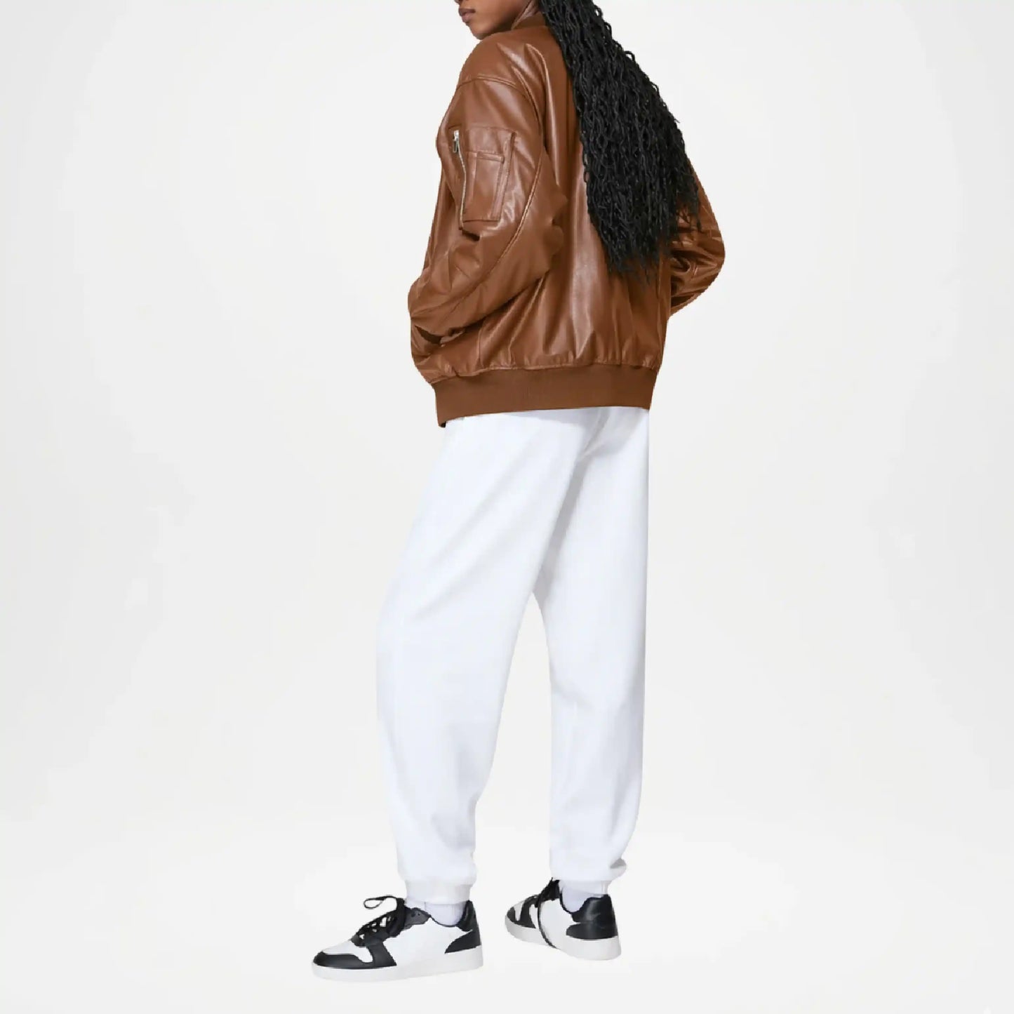 Person wearing a brown leather jacket and white pants on a white background
