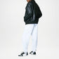 Person wearing a black leather jacket, white pants, and black sneakers