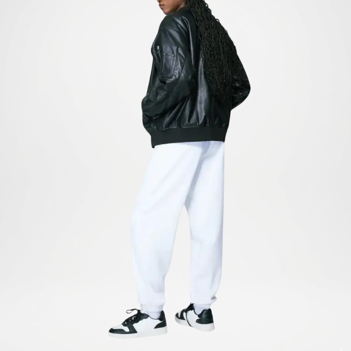 Person wearing a black leather jacket, white pants, and black sneakers