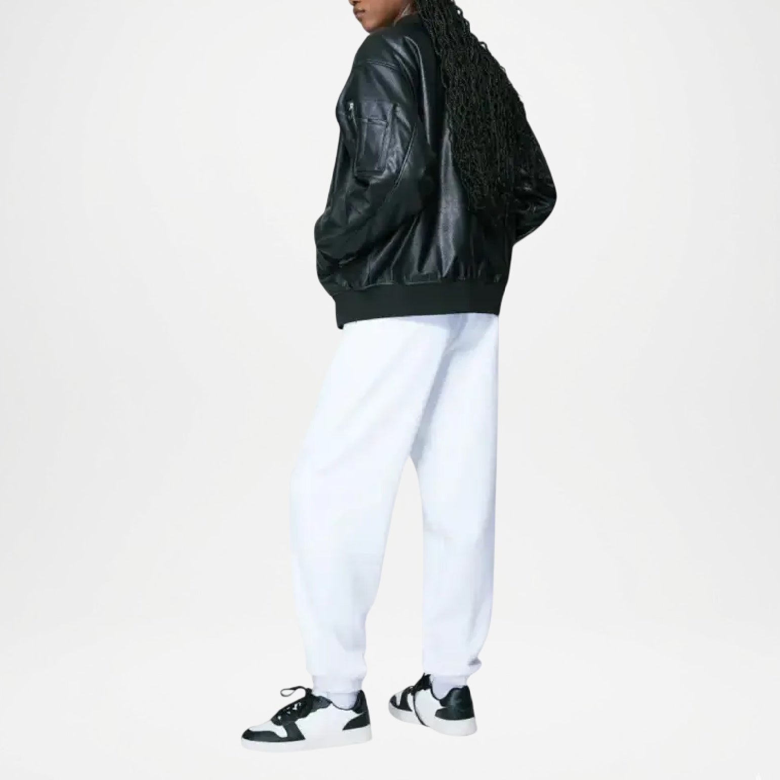 Person wearing a black leather jacket, white pants, and black sneakers