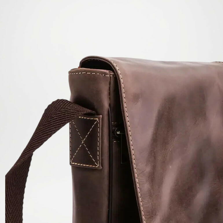 Brown leather bag with a strap on a light gray background
