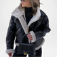 Woman wearing a black leather jacket with white fur lining, holding a black handbag.