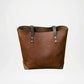 Brown leather tote bag with black straps on a light gray background