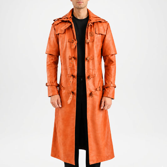 A model wearing a long, double-breasted orange leather trench coat over a black outfit, photographed against a plain white studio background.