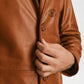 Close-up of a brown leather jacket with a brand logo, featuring a hand adjusting the sleeve.